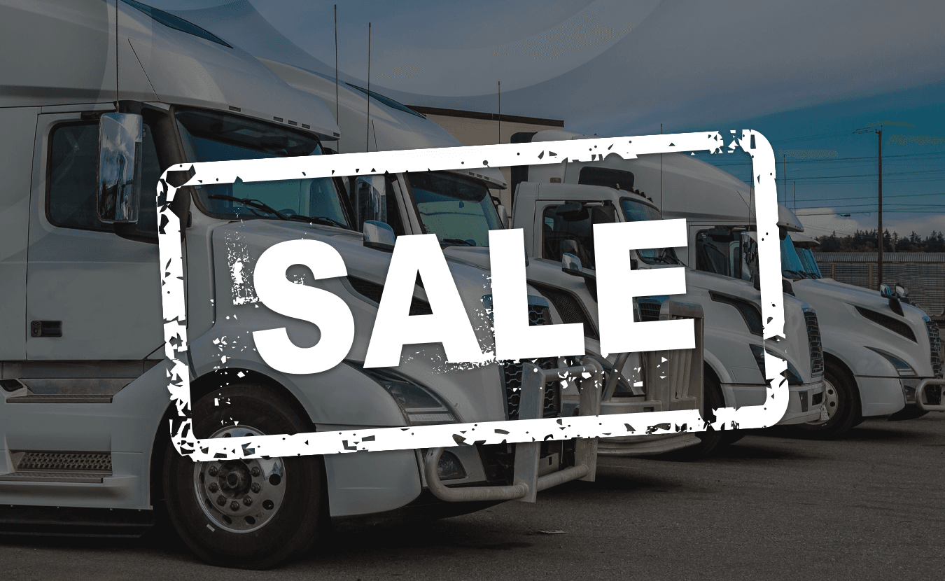 Row of white semi trucks parked at a dealership with a bold ‘SALE’ stamp over the image.